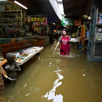 A Shop Owner Wades Through Floodwaters Inside A Market, Highlighting The Immediate Economic And Cultural Toll On Small Businesses.