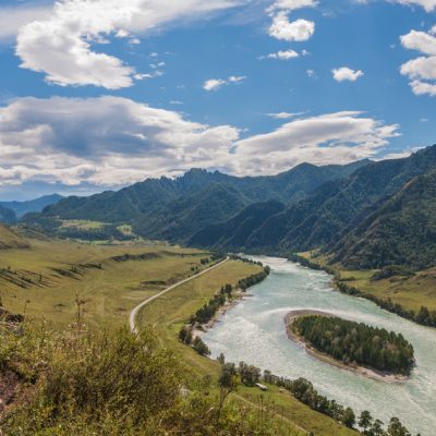 Mountain landscape with a river, island in the middle of the river, the trees along the banks, fields, road. View from the mountain.